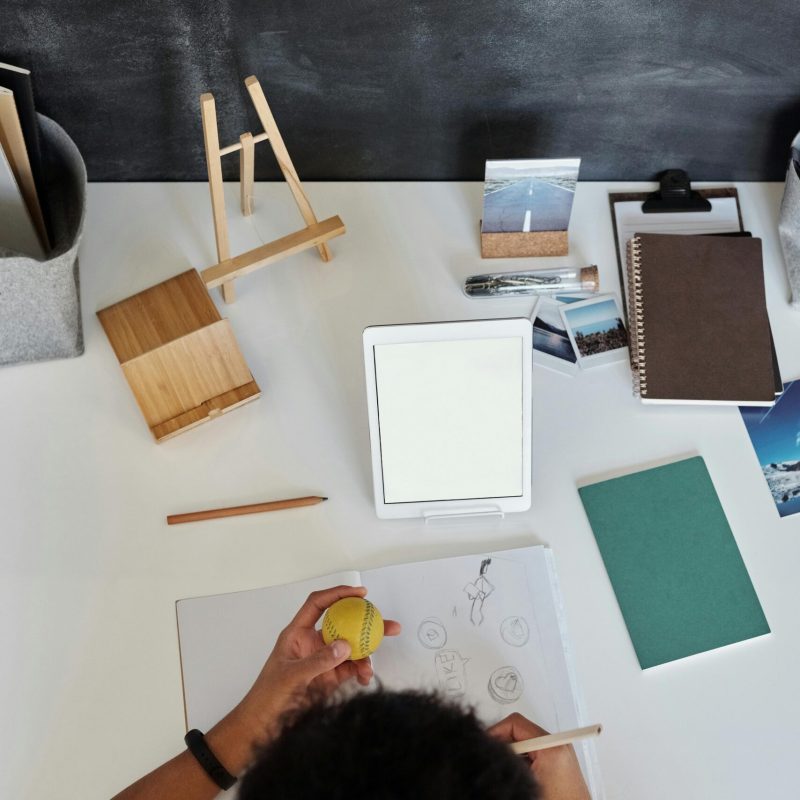 pexels-photo-4144097-4144097 Overhead view of a teenager drawing at a desk with art supplies and tablet.